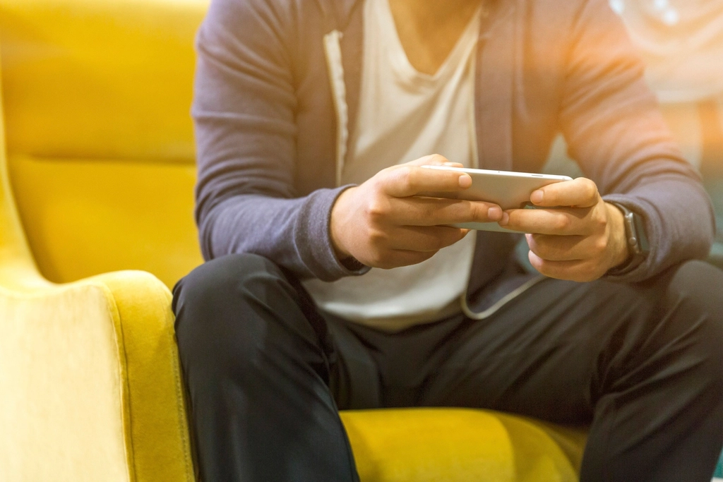 A man sitting on a yellow sofa holding a smartphone in both hands