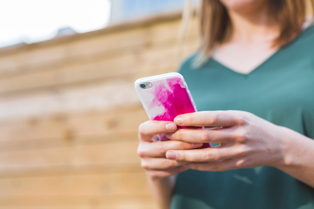 A woman in a green top holding a smartphone with a pink case
