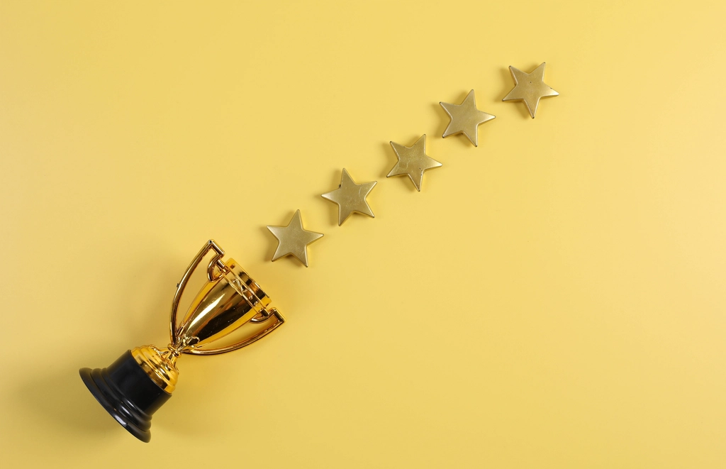 A small gold trophy and a row of five gold stars on a yellow background