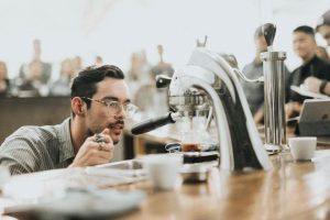 A man in glasses watching espresso pour at a busy coffee bar
