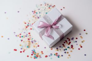 A white gift box tied with a pink ribbon, surrounded by confetti