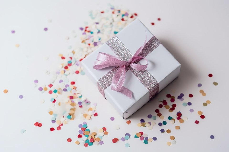 A white gift box tied with a pink ribbon, surrounded by confetti