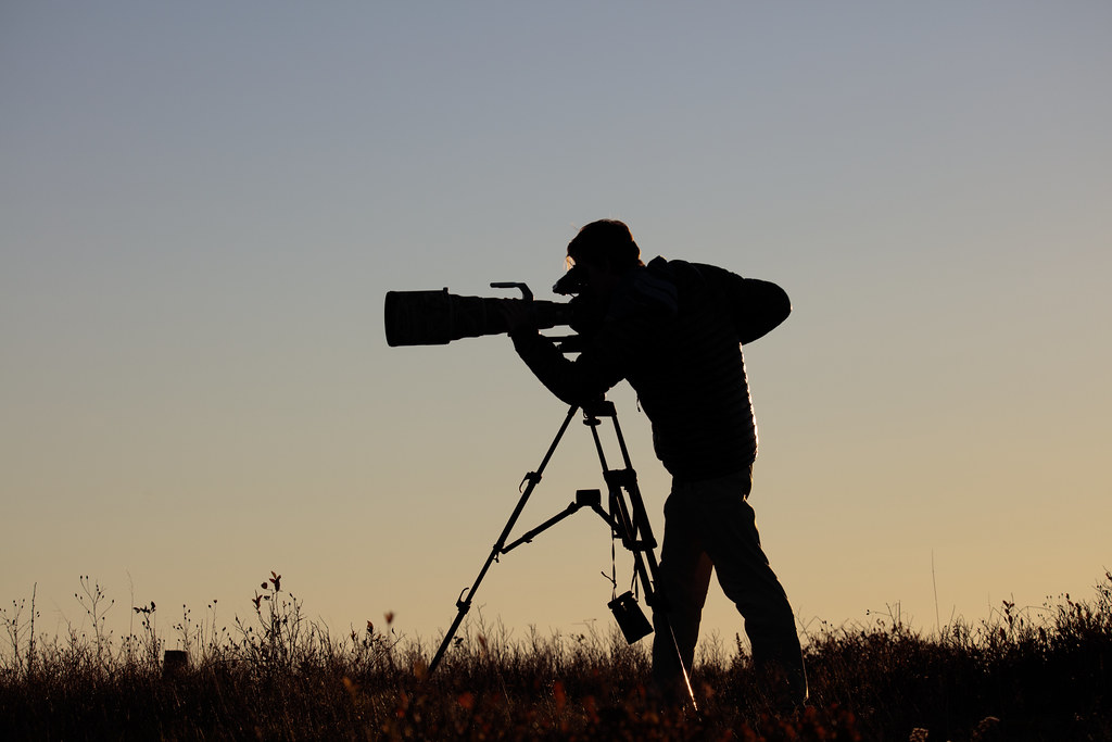 The silhouette of a person with a camera on a tripod at sunset