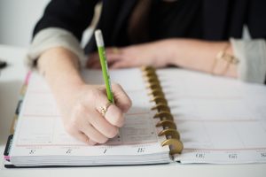 A woman writing in a ring-bound weekly planner with a green pencil