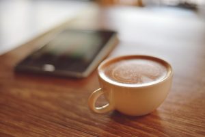 A smartphone lying on a wooden table beside a cup of coffee